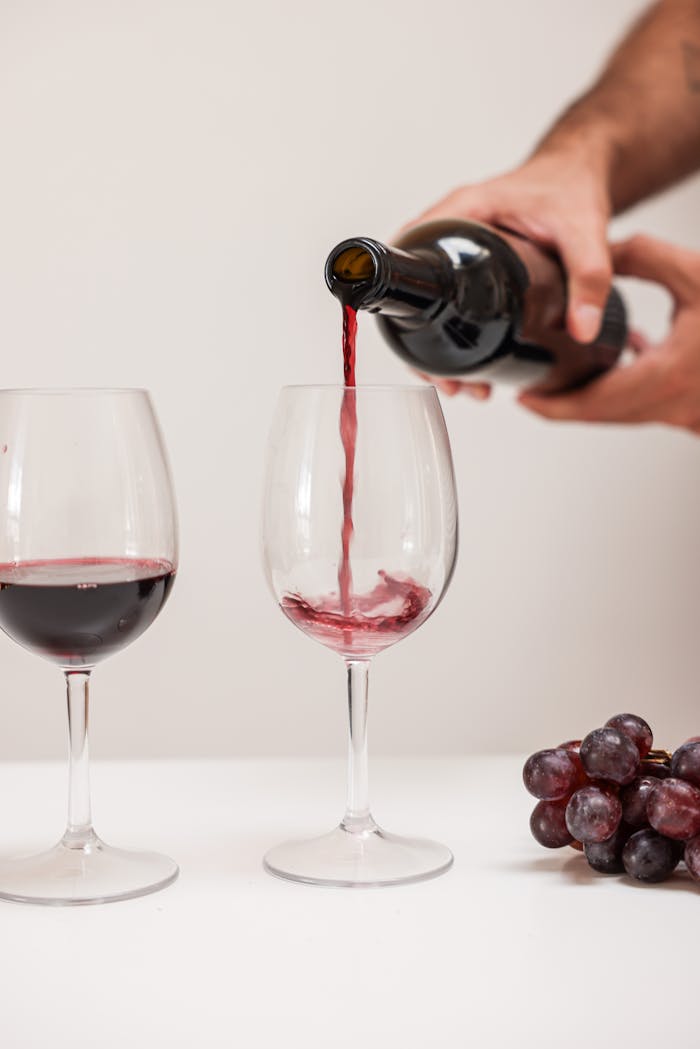 Red wine being poured into glass with grapes on table; a classic wine tasting scene.