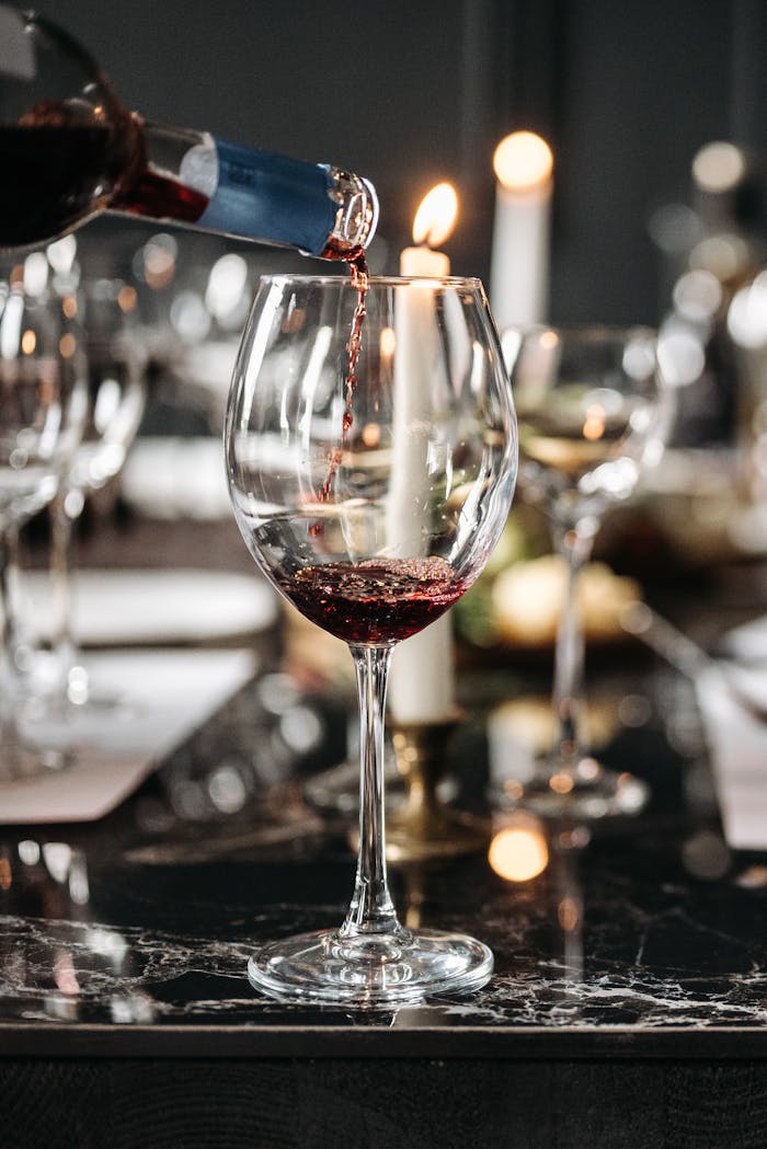 Elegant red wine pouring into a glass on a candlelit dining table setting. Perfect for romantic or culinary themes.