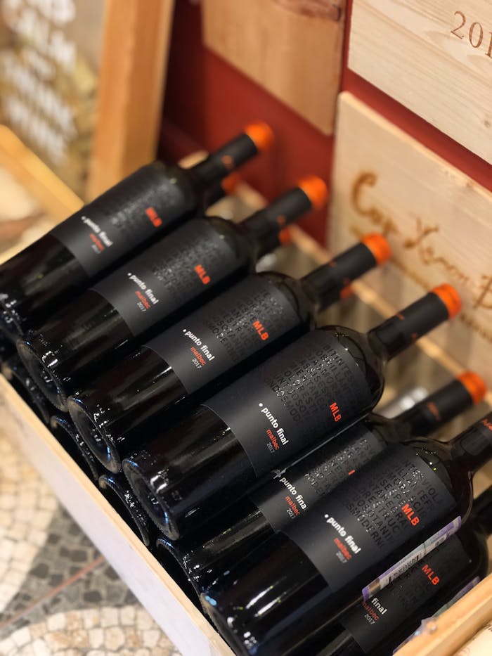 A close-up high angle view of red wine bottles displayed in a wooden crate, highlighting detailed labels.